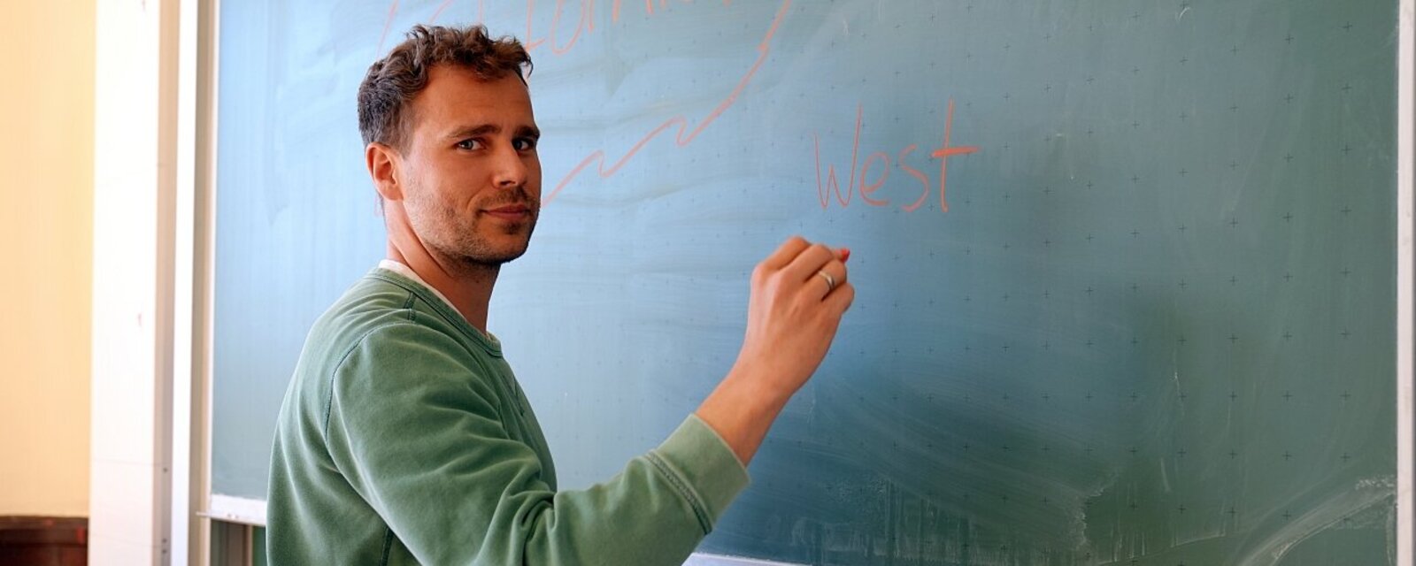 Auf dem Bild ist eine Lehrkraft zu sehen, die im Rahmen der Schulpraktische Studien Lehrkräfte betreut. Sie steht an einer Tafel.