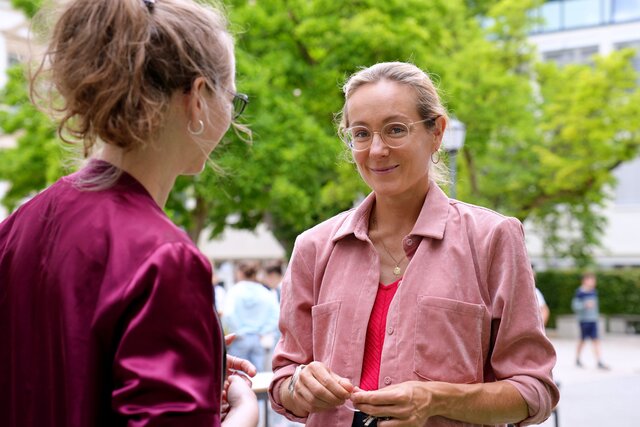 Zu sehen ist Alumna Luisa Brass (von vorne und in die Kamera lächelnd) im Gespräch mit Alumni-Managerin Alexandra Gräber (von hinten).