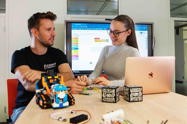 Ein junger Mann und eine junge Frau sitzen am Tisch. Auf diesem liegen diverse Medienprodukte.