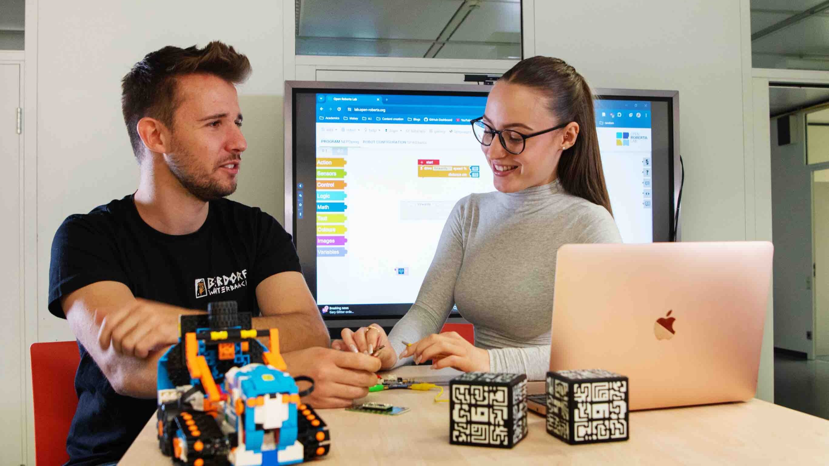 Ein junger Mann und eine junge Frau sitzen am Tisch. Auf diesem liegen diverse Medienprodukte.
