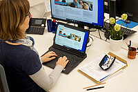 Auf dem Foto ist Jutta Johnson schräg von hinten zu sehen. Sie sitzt am Laptop und arbeitet an der Website des AW-ZIB.