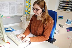 Frau vor einem Computer und sie hat ein Headset auf dem Kopf.