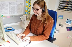 Frau vor einem Computer und sie hat ein Headset auf dem Kopf. 