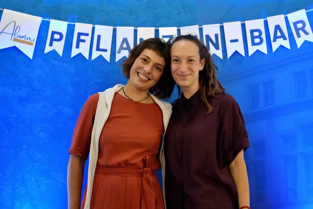 Zu sehen sind zwei Frauen, die nebeneinander vor einer blauen PHHD-Messewand stehen. An der Wand hängt eine Wimpelkette mit dem Schriftzug „Pflanzenbar“.