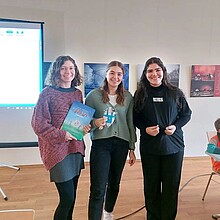 Drei Studentinnen stehen vor einem Beamer mit Buch