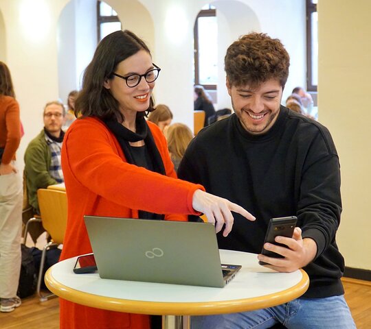 Zu sehen sind 2 stehende Personen vor einem Laptop