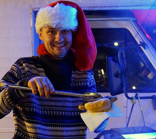 Zu sehen ist Student Tim Strahl mit einer Weihnachtsmütze und Bratwurst in der Hand.