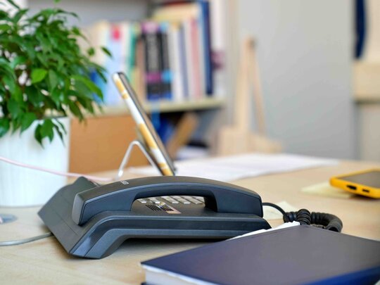 Ein Telefon auf einem Schreibtisch, im Hintergrund ein Bücherregal im Altbau der Pädagogischen Hochschule Heidelberg.