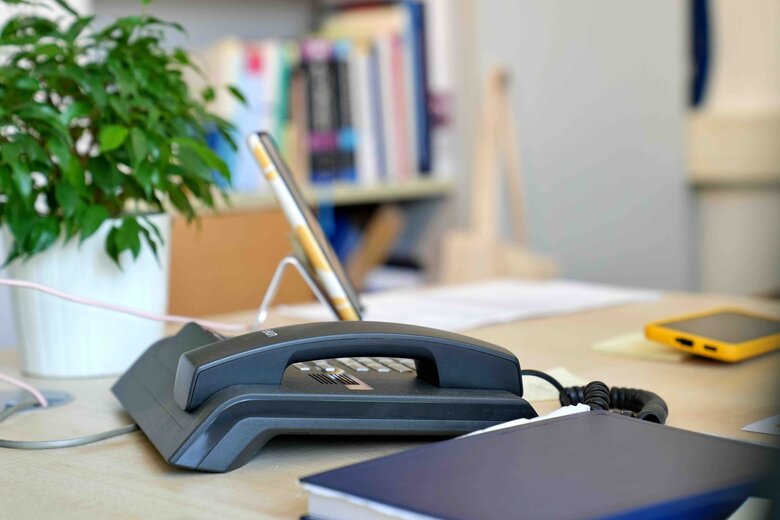 Ein Telefon auf einem Schreibtisch, im Hintergrund ein Bücherregal im Altbau der Pädagogischen Hochschule Heidelberg.