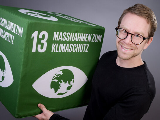 Das Bild zeigt den Klimamanager Johannes Rüd mit einen Klimaziel-Würfel.