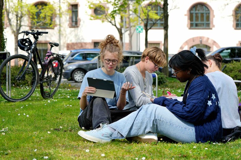 4 Studierende der Pädagogischen Hochschule Heidelberg sitzen mit Laptops und Tablets auf einer Wiese.