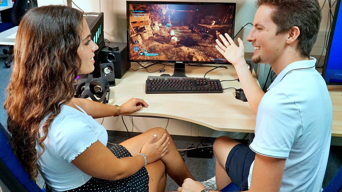 Zwei Personen unterhalten sich vor einem Bildschirm.