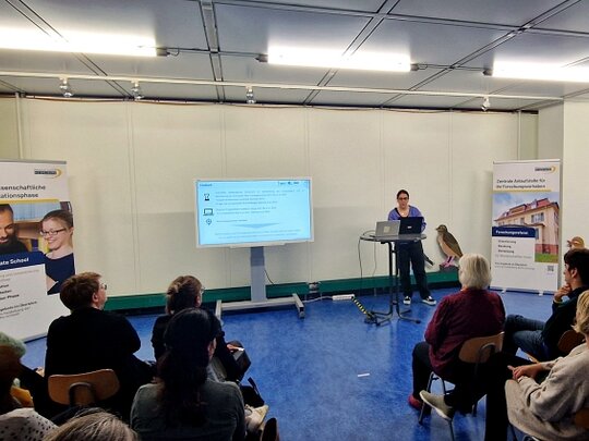 Zu sehen ist eine Rednerin vor dem Auditorium