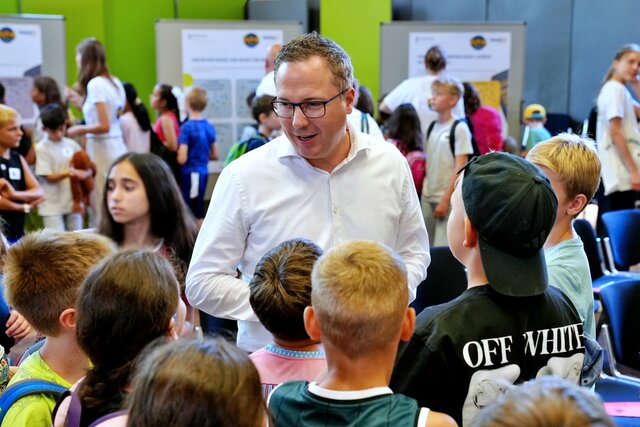 Staatssekretär Deuschle in Mitte von zahlreichen Kindern. Aufgenommen wurde das Bild während des Kinderparlaments in der Festhalle der Pädagogischen Hochschule Heidelberg.