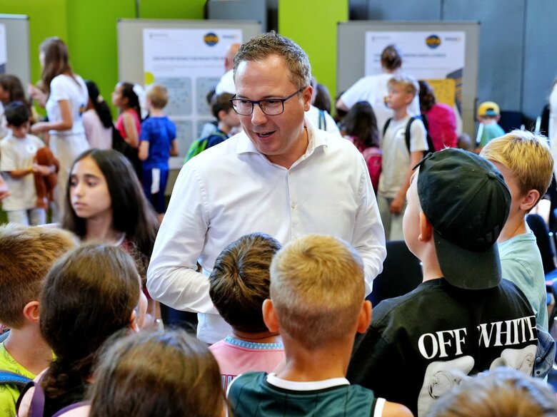 Staatssekretär Deuschle in Mitte von zahlreichen Kindern. Aufgenommen wurde das Bild während des Kinderparlaments in der Festhalle der Pädagogischen Hochschule Heidelberg.