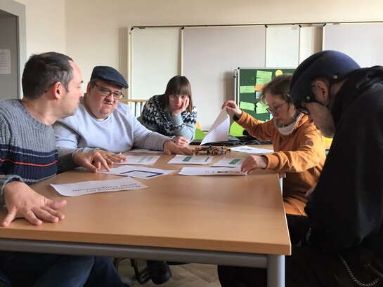 Das Foto zeigt fünf Bildungsfachkräfte um einen Tisch sitzen. Auf dem Tisch sind unterschiedliche Zettel verteilt.