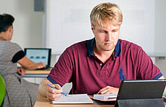 Das Foto zeigt einen Studierenden am schreiben vor seinem Tablet.
