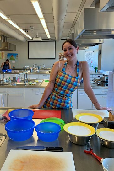 Eine Studentin der Alltagskultur und Gesundheit mit Schürze steht in der Lehrküche vor verschiedenen Schüsseln.