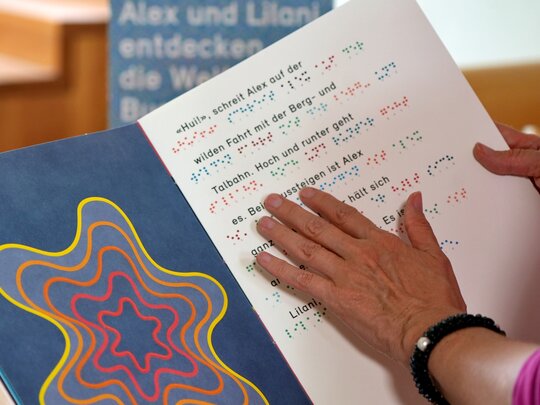 Das Bild fokussiert die Hand einer Person. Sie liest ein Buch in Brailleschrift.