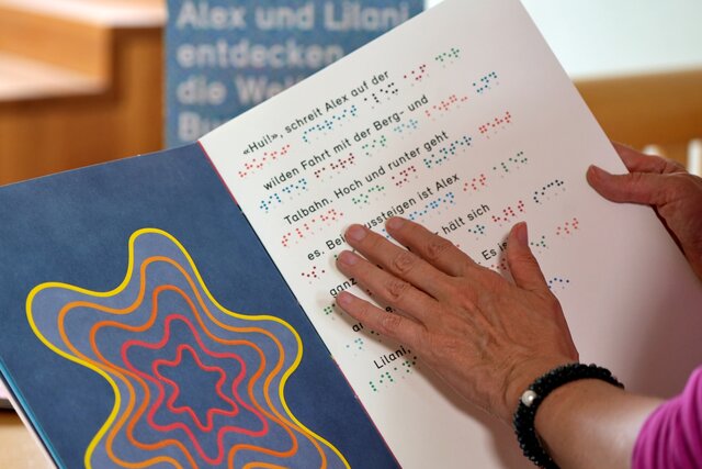 Das Bild fokussiert die Hand einer Person. Sie liest ein Buch in Brailleschrift.