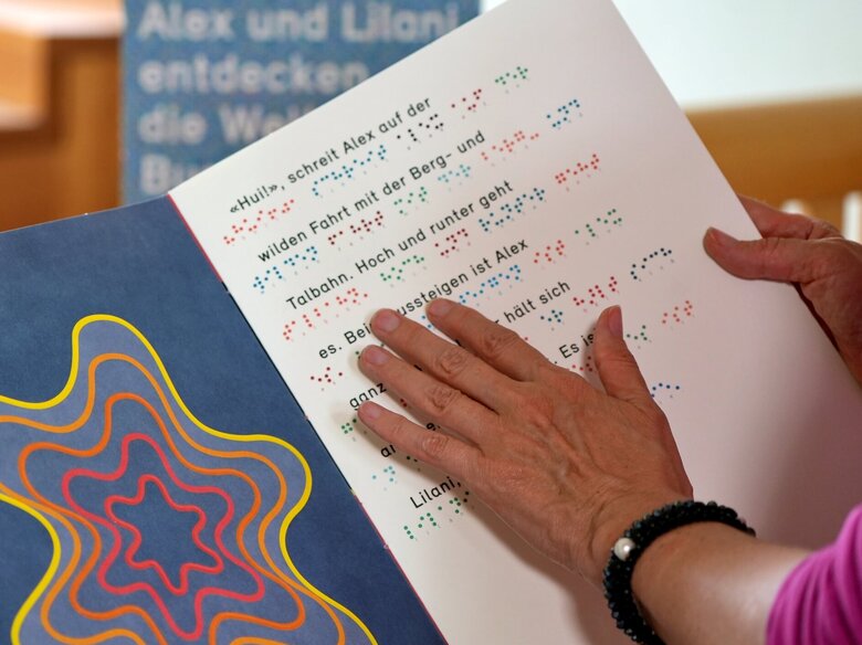 Das Bild fokussiert die Hand einer Person. Sie liest ein Buch in Brailleschrift.