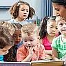 Das Bild zeigt eine Frau, die mehreren Kindern etwas vorliest.