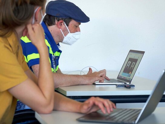Das Bild zeigt zwei Menschen vor jeweils einem Laptop.