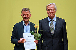 Markus Lang und Karl-Heinz Dammer. Lang hat die Lehrpreis-Urkunde und eine gelbe Rose in der Hand. Beide schauen freundlich in die Kamera.