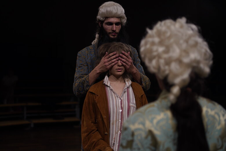 Studierende der Theaterpädagogik in einer Aufführung: Momo spricht mit Meister Hora. Der andere Meister Hora steht hinter ihr und hält ihr die Augen zu.