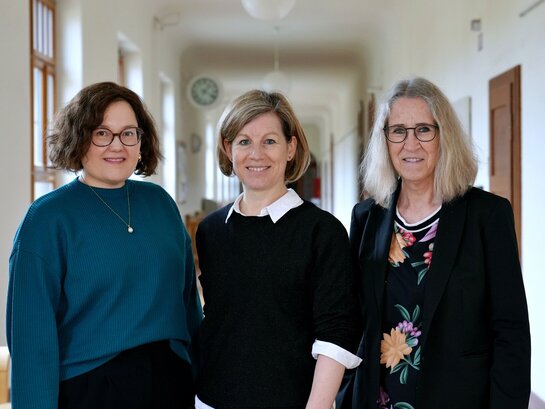 Das Foto zeigt drei Personen in die Kamera lächeln.