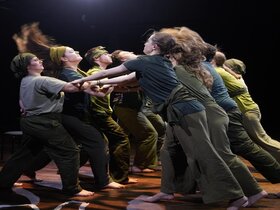 Zu sehen sind Menschen auf der Bühne, deren Arme ineinander verwoben sind