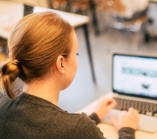 Junge Frau sitzt am Laptop und tippt