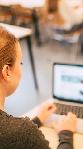 Junge Frau sitzt am Laptop und tippt