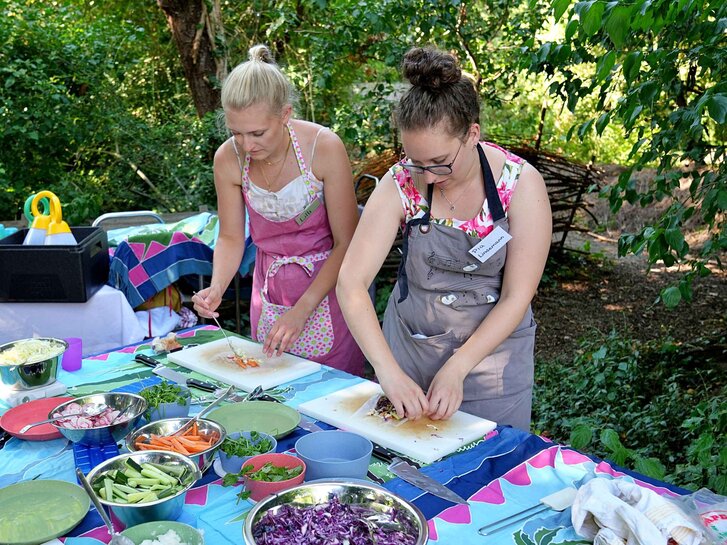 Zwei Studentinnen stehen im Ökogarten und stellen Sommerrollen her.
