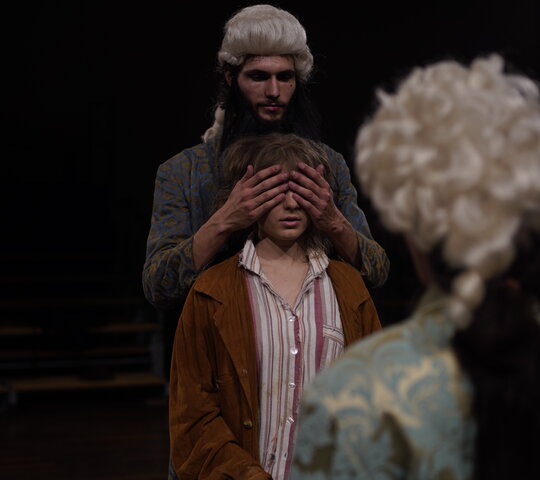 Studierende der Theaterpädagogik in einer Aufführung: Momo spricht mit Meister Hora. Der andere Meister Hora steht hinter ihr und hält ihr die Augen zu.
