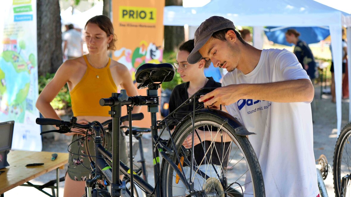 Ein junger Mann arbeitete an einem Fahrrad. Im Hintergrund sieht man weitere Personen sowie Stände des Future Festivals.