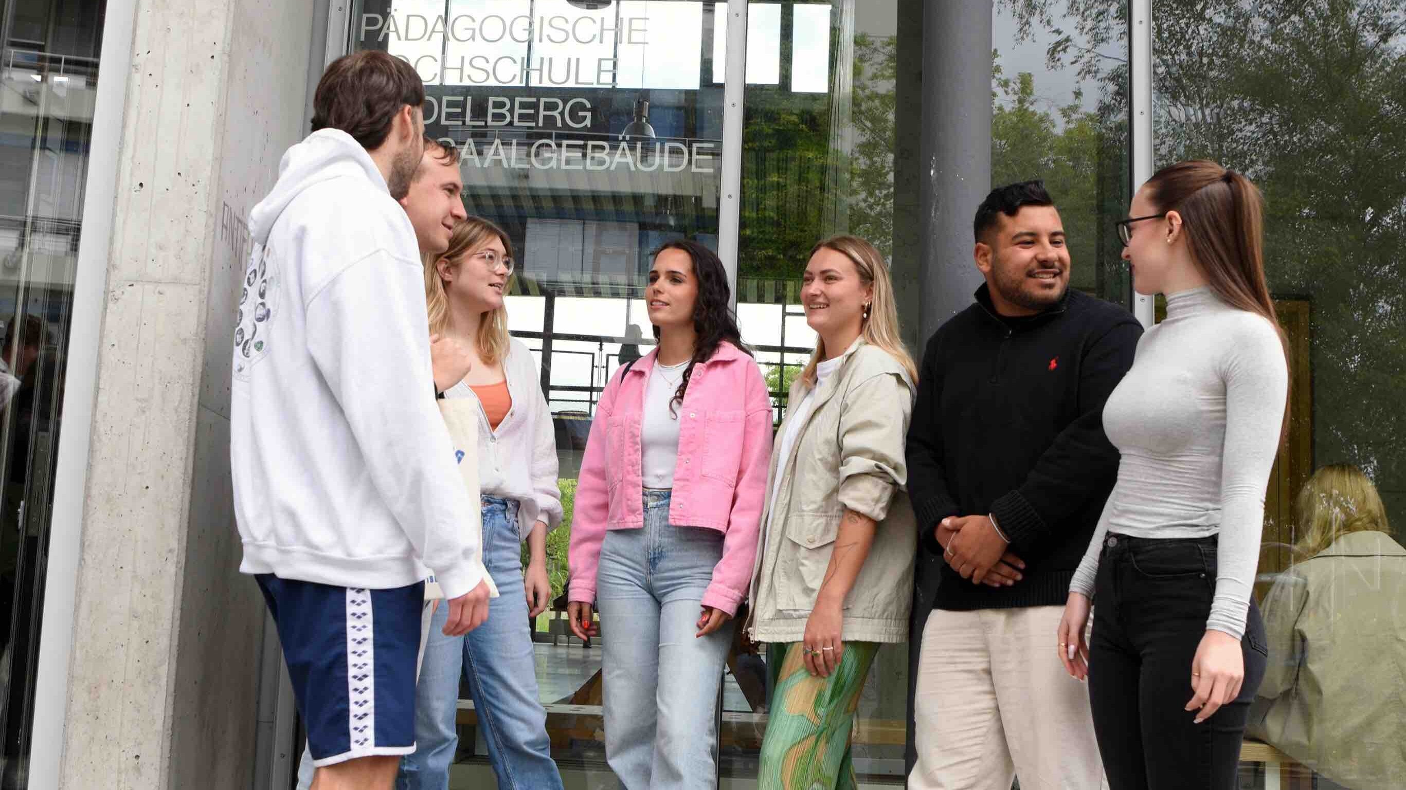 Eine Gruppe von Studierenden steht vor dem Hörsaalgebäude und unterhält sich.