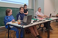 Das Bild zeigt Louisa Kabbe und Susann Bensch bei ihrer Modulprüfung. Sie sitzen bzw. stehen vor einer Tafel in einem Seminarraum der PH Heidelberg. Mit dabei auf dem Bild sind FSJ-Kraft Carl Hoffmann sowie Bildungsfachkraft Helmuth Pflantzer.