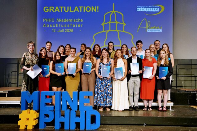 Zu sehen sind Absolvent:innen der PHHD, die sich mit ihren Urkundenmappen auf der Bühne zum Gruppenfoto aufgestellt haben.
