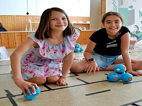 Zu sehen sind zwei Mädchen, die auf dem Boden sitzen und Dash-Roboter bewegen