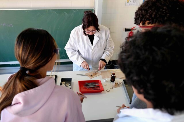 Eine Lehrperon führt ein Experiment durch, Studierende beobachten sie dabei