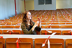 Studentin sitzt alleine in einem Hörsaal und gebärdet mit den Händen