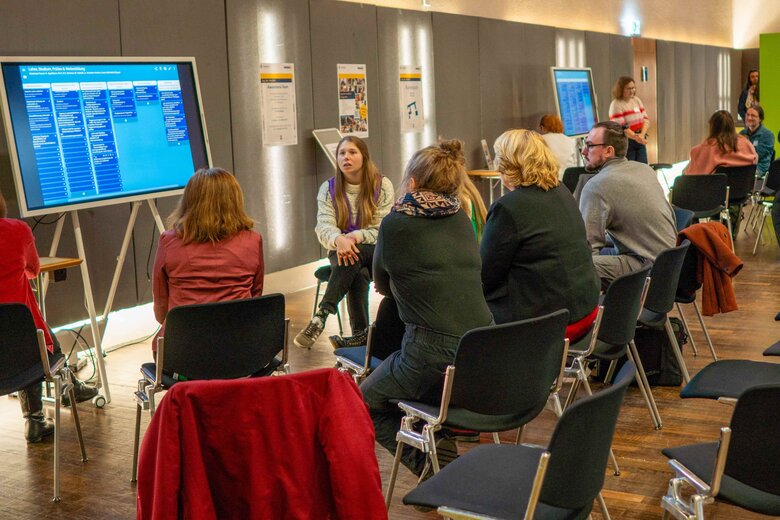 Das Bild zeigt Mitglieder der PH Heidelberg, die gemeinsam am Tag der Vielfalt diskutieren. Unterschiedliche Menschen sitzen im Halbkreis um einen größeren Monitor.
