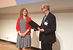 Auf dem Bild ist zu sehen, wie Christian Wiesmüller die Urkunde an Laura Arndt übergibt.