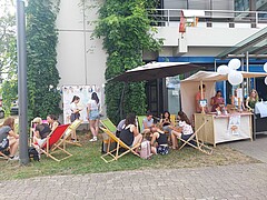 Bild zeigt Liegestühle, in denen Studierende sitzen und sich unterhalten. Rechts davon ist ein Stand mit einer Bar des Teams von RethinkyourHDrink.