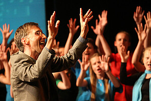 Dr. Detterbeck als Chorleiter mit Chor Hände in der Höhe, lachend