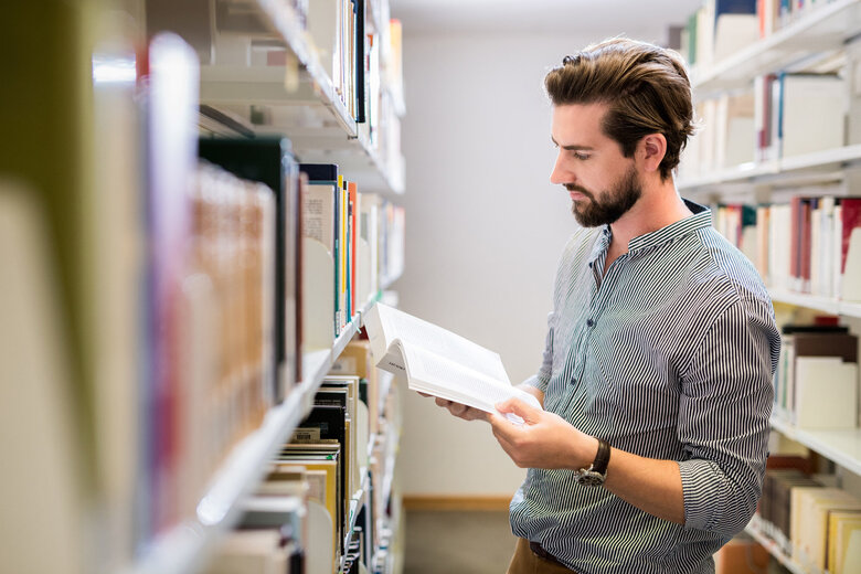 Zu sehen ist ein Student in einer Bibliothek. 