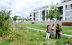 Auf dem Symbolbild sieht man unten rechts eine Gruppe von vier Studierenden, die im Kreis stehen und etwas betrachten. Den Großteil des Bildes nimmt die Bahnstadt, ein Stadtviertel in Heidelberg ein. Copyright: PH Heidelberg