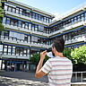 Auf dem Bild ist ein Student von hinten zu sehen. Er zieht sich gerade eine Maske auf und läuft auf den Neubau der Hochschule zu. Copyright: PH Heidelberg.