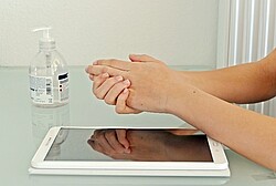 Das Bild zeigt jemanden, der sich seine Hände über einem Tablet desinfiziert.